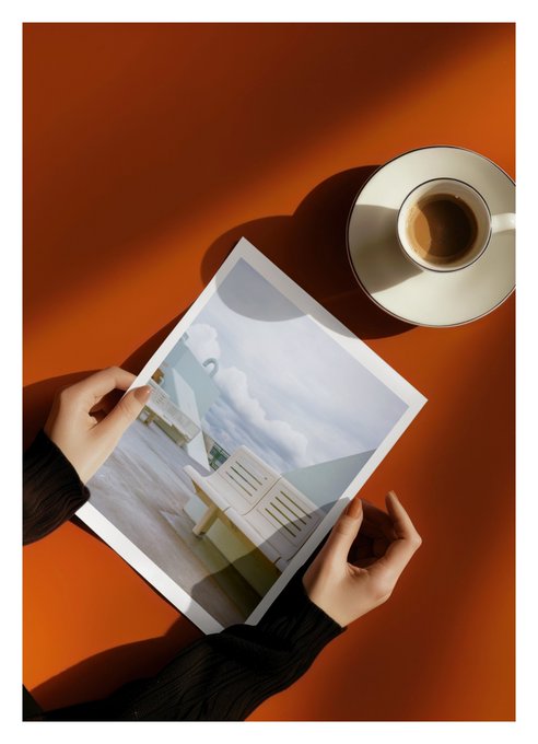 The image shows a person holding a magazine with an interesting picture of a building, possibly a house or apartment complex, while sitting at a table next to a cup of coffee and a saucer. The scene appears to be set against an orange background, which adds a warm and inviting atmosphere to the setting. The post features a photo of this person's hands holding the magazine with the picture on it, along with some text that reads "SOLD The first edition of “The Quiet Deck” has been collected by @cdxart for 9 editions remain transient." This suggests that the image might be related to an art project or a personal collection.