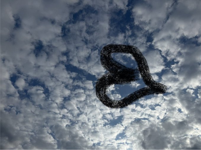 A heart-shaped smoke ring floating against a backdrop of blue sky and scattered white clouds.