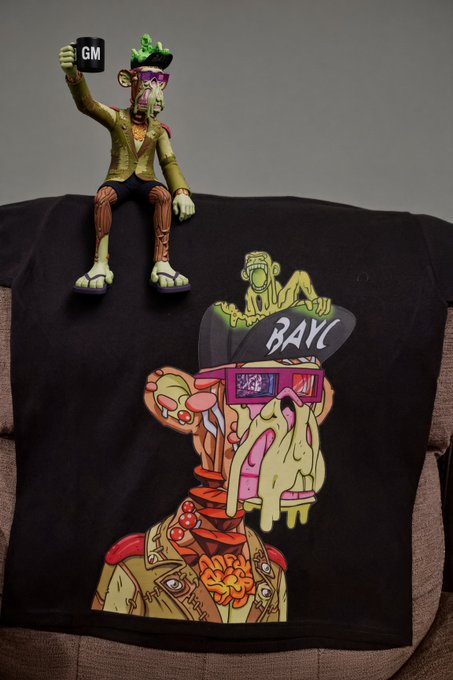 A black t-shirt features a colorful graphic of a melting zombie-like figure wearing 'BAYC' Bored Ape Yacht Club sunglasses, with a matching vinyl figure sitting on top of the shirt.
