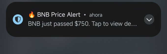 A push notification alert from a shield icon reads 'BNB Price Alert • ahora: BNB just passed $750. Tap to view de...'