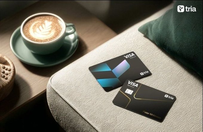 The image shows a coffee cup with a latte art design sitting next to two Visa cards placed on top of a couch cushion. The scene suggests that someone might be enjoying their coffee while checking or using their credit cards for purchases, possibly online shopping or dining out at a restaurant. The focus on the coffee and cards indicates that these items are important aspects of the person's daily life or leisure activities.