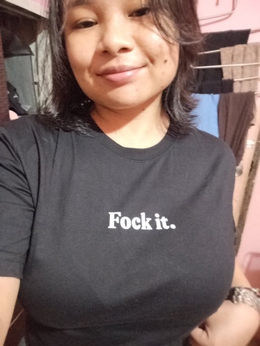 A selfie of a smiling young woman wearing a black t-shirt with the humorous text 'Fock it.' printed in white.