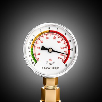 A close-up of an analog pressure gauge with a white face and a brass base, featuring green, yellow, and red color-coded zones and scales in 'psi' and 'bar'.