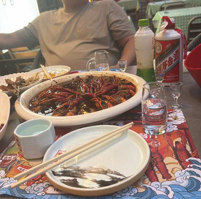 A person sits at a table with a large platter of crawfish, a bottle of Moutai (贵州茅台酒) baijiu, and empty plates with chopsticks. The image appears unrelated to the trading post, as it depicts a casual meal rather than any financial content.

This is misleading. The image shows a crawfish dinner, not anything related to altcoin trading or group chats.