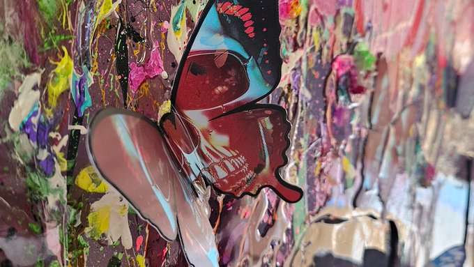 A close-up of a butterfly-shaped cutout covered in dripping, multicolored paint splatters.