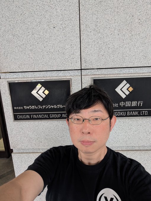 A man with glasses takes a selfie in front of plaques displaying the logos of Chūgin Financial Group, Inc. (ちゅうぎんフィナンシャルグループ) and Shingoku Bank, Ltd. (中国銀行), connecting to his post about visiting Chūgin and the early investment decision made by its subsidiary, Chūgin Capital.
