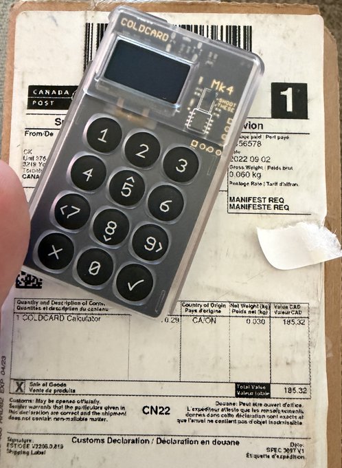 A hand holds a transparent Coldcard Mk4 hardware wallet over a Canada Post customs declaration form showing 1 unit of a "COLDCARD Calculator" shipped from CA-CN with a total value of $185.32 CAD, illustrating the issue of the Bitcoin wallet arriving in packaging that explicitly identifies it as a cryptocurrency device on a customs declaration.