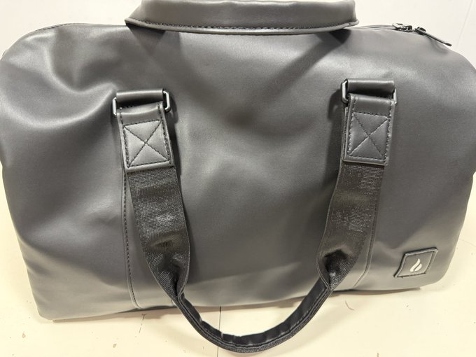A gray travel duffel bag with black handles and a small logo tag rests on a light surface.