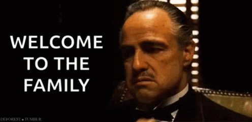 The image features a man dressed in a tuxedo, sitting down with his arms crossed over his chest. The text "Welcome To The Family" is written above him, indicating that he has been welcomed into the family. The background of the image is dark and out of focus, drawing attention to the man and the message on the poster.
