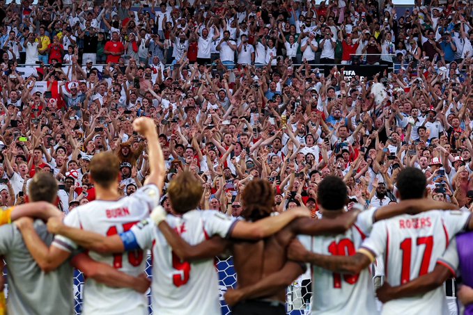 England soccer players, including #17 "ROJERS" and #5 "BURN," stand arm-in-arm facing a massive, jubilant crowd of fans with raised arms and fists in a moment of unified celebration. The image's theme of passionate collective support and rallying behind a team parallels the XRP Army's message of solidarity and shared conviction in the post.
