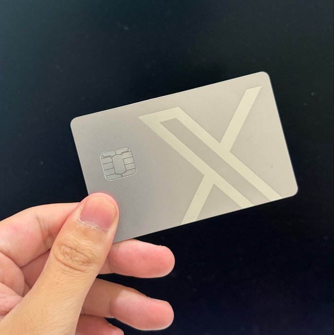 A hand holding a sleek silver metal payment card featuring an embedded EMV chip and a stylized 'X' or 'A' design.