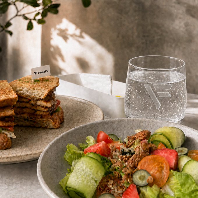 A food photography shot featuring a sandwich with a "Farmez" flag, a fresh salad with cucumber, tomatoes, and lettuce, and a glass of water with a Farmez logo embossed on it.