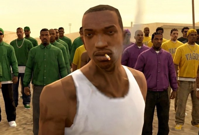A video game screenshot, likely from GTA San Andreas, showing a man in a white tank top smoking a cigarette with a crowd of people wearing green, purple, and yellow shirts behind him.