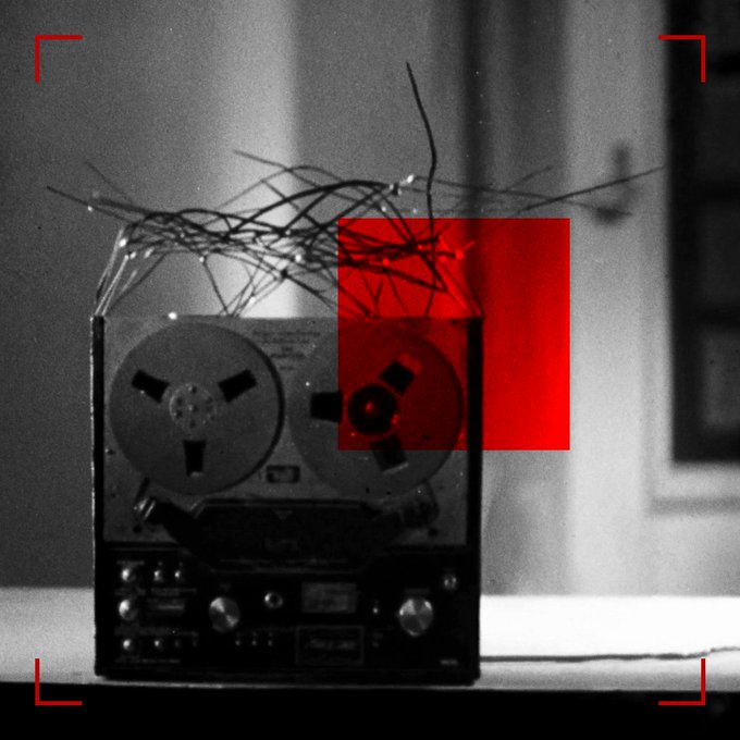 A vintage reel-to-reel tape recorder sits on a surface with tangled wires on top, overlaid with a red rectangle and corner brackets.