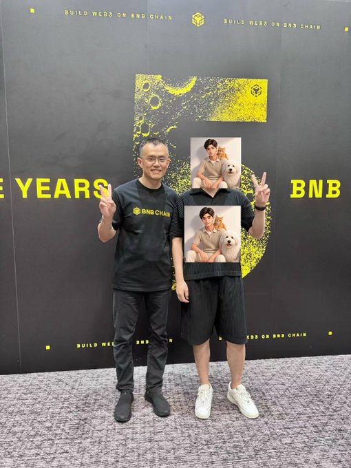 Two men pose in front of a '5 YEARS' BNB Chain backdrop celebrating the anniversary; one wears a BNB Chain t-shirt and the other holds up two photos of himself with a white dog.