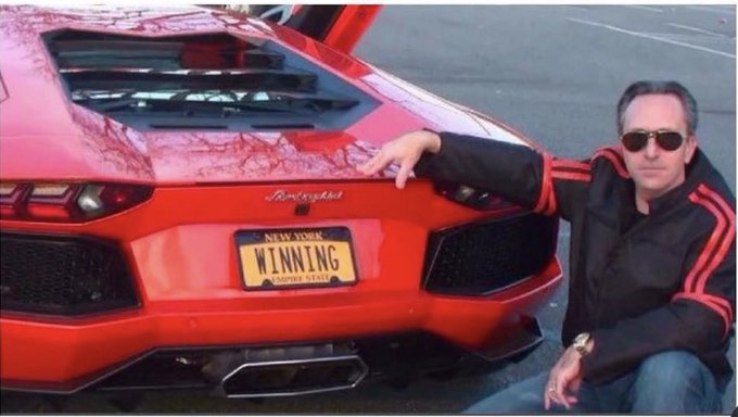 A man in sunglasses poses proudly beside a sleek red sports car featuring a New York "WINNING" license plate, humorously suggesting that even a small $8 profit on Bitcoin feels like a major financial triumph worthy of flexing like a high-roller.