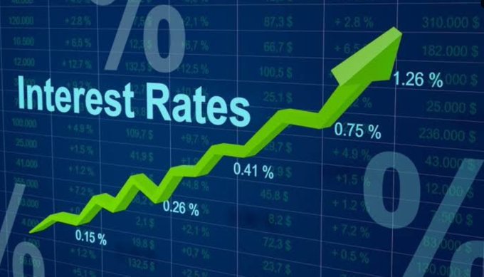 Graphic illustration titled "Interest Rates" showing a green upward-trending zigzag arrow over a dark blue background filled with various dollar figures and percentage values like 0.26%, 0.41%, 0.75%, and 1.26%.