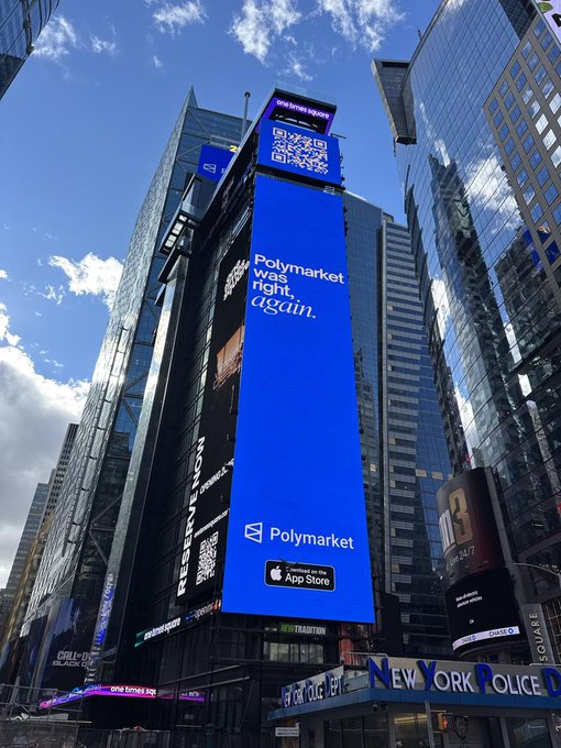 A large blue digital billboard in Times Square displays a QR code above the text 'Polymarket was right, again.' along with the Polymarket logo and an App Store badge.