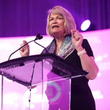 Senator Cynthia Lummis speaks passionately at a podium during an event with a purple-lit backdrop, illustrating her role in sharing an updated CLARITY Act draft containing over 100 Democratic-requested changes.