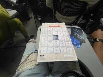 First-person view looking down at a person's lap, showing a folded instruction paper or map with icons and diagrams on their jeans.