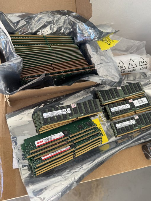 A box filled with silver colored computer parts sits on a table, including multiple DRAM and DDR4 RAM sticks as well as some components for a computer.