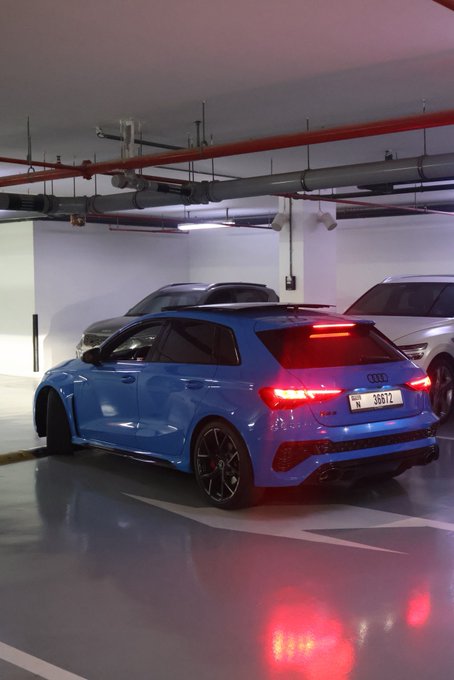 A blue Audi hatchback with illuminated taillights is parked in an indoor garage, with other vehicles visible in the background. The license plate reads "38872" and the "GN" caption likely refers to the sporty Audi RS3, a popular choice among automotive enthusiasts.