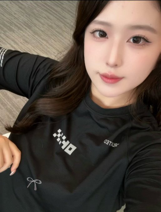 A young woman with long dark hair wearing a black PUMA long-sleeve athletic top takes a close-up selfie.