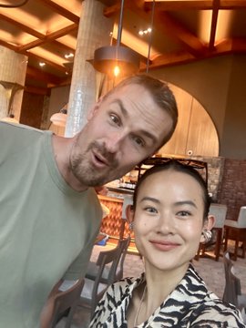 A selfie of a man and a woman posing together in what appears to be a restaurant or bar setting with warm lighting.