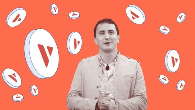 A man speaks in front of an orange background filled with floating white coins bearing a red play-button symbol resembling a cryptocurrency logo.