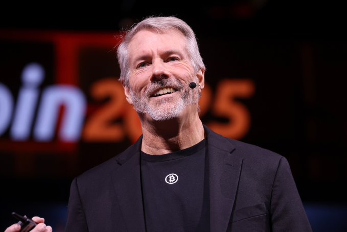 Michael Saylor, founder of MicroStrategy, smiles while speaking at a conference with "in 2025" visible in the backdrop, accompanying his bold claim that his company aims to become the world's most valuable company by market cap.