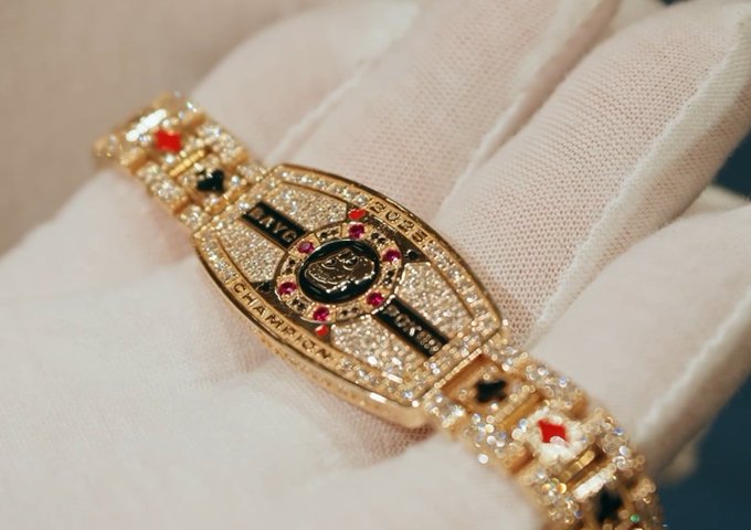 Close-up of a luxury gold bracelet covered in diamonds and colored gemstones, featuring a Louis Vuitton design element on a gloved hand.
