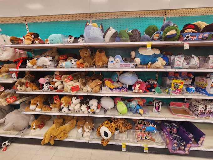 A store display shelf features a large assortment of stuffed animals, plush toys, and a box of Harry Potter merchandise arranged on multiple tiers.