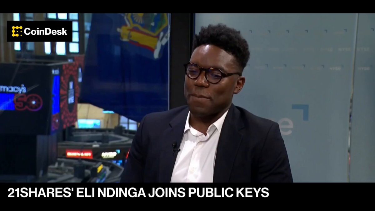 The image shows a man wearing glasses, sitting at a desk, and talking into a microphone. The background of the image features a TV screen displaying a news segment about the Hyper Liquid company. The text "21shades" and "Elinkinga Joins Public Keys" are also visible in the image.