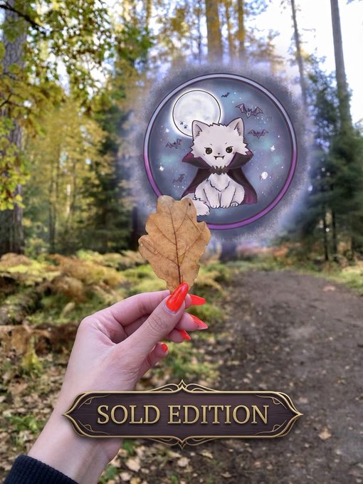 A hand holding an oak leaf with a circular fantasy vampire cat sticker design overlaid, labeled 'SOLD EDITION' in a forest setting.