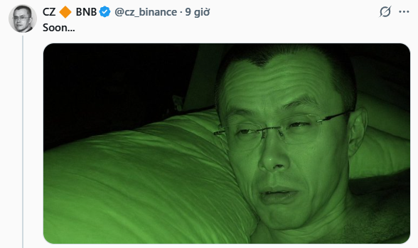 A tweet from CZ 🔶 BNB (@cz_binance) with the text 'Soon...' showing a green-tinted selfie of a man with glasses lying down.