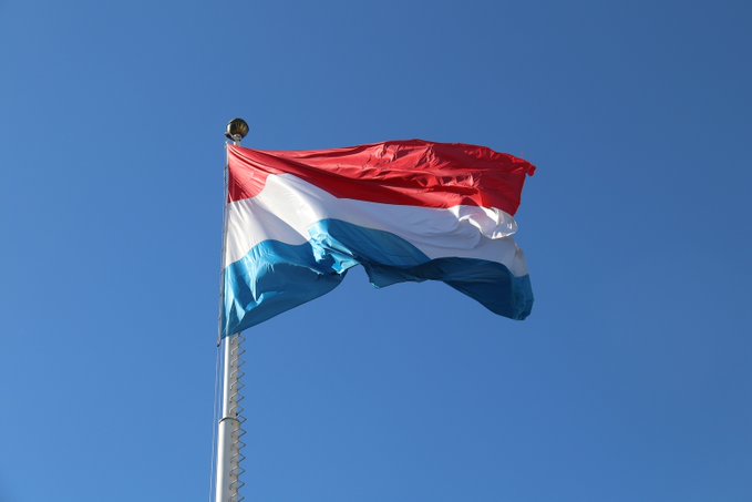 A Luxembourg flag waves against a clear blue sky, symbolizing the nation as its new anti-fraud law comes into effect this Saturday. The image represents Luxembourg's stance in combating fraud, particularly empowering the Financial Intelligence Unit to notify banks and crypto exchanges about suspicious accounts.