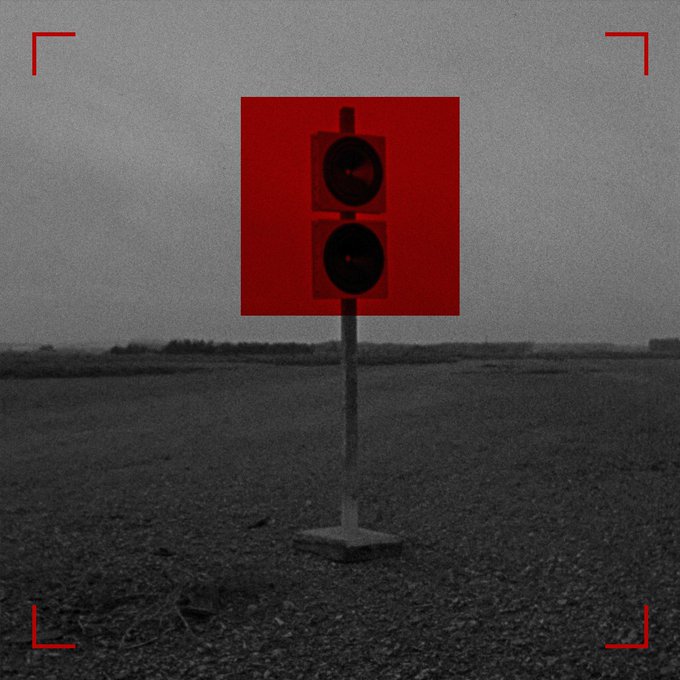 A dark, grainy image of a road signal on a pole in an empty field, with a red highlight box framing the signal and red corner markers overlay the image.