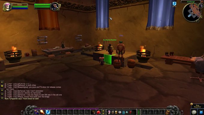 This is a screenshot from the video game World of Warcraft, showing the interior of a tavern or inn with characters gathered around a table near a fire pit, with an Auctioneer npc visible. The image relates to the "imagine trading memecoins from here" caption by presenting this rustic in-game tavern setting as an absurd, fantasy-world alternative workspace for cryptocurrency trading, with the chat box showing trade messages and player Myla Tymgraine advertising "Fresh bread for sale!"