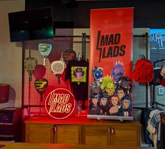 A brightly lit Mad Lads merchandise display features red banners and various branded items including a neon sign, arranged on a counter.
