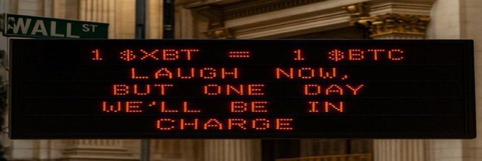 An LED sign on Wall St displaying the message in red text: "1 XBT = 1 BTC. LAUGH NOW, BUT ONE DAY WE'LL BE IN CHARGE."