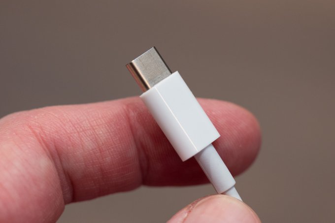 A close-up shows a USB‑C cable connector being held between fingers, emphasizing the need to inspect cables before plugging them into a hardware wallet.