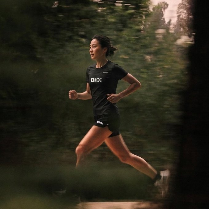 A woman wearing ON running apparel sprints through a forest trail.