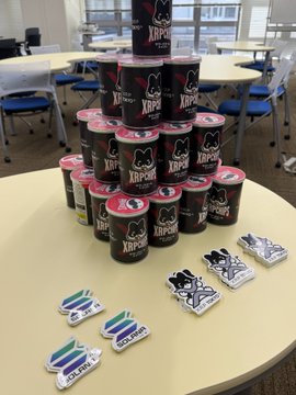 A pyramid of Kippy branded ice cream containers sits on a yellow table surrounded by some packaged snacks and stickers, with office chairs and desks in the background.