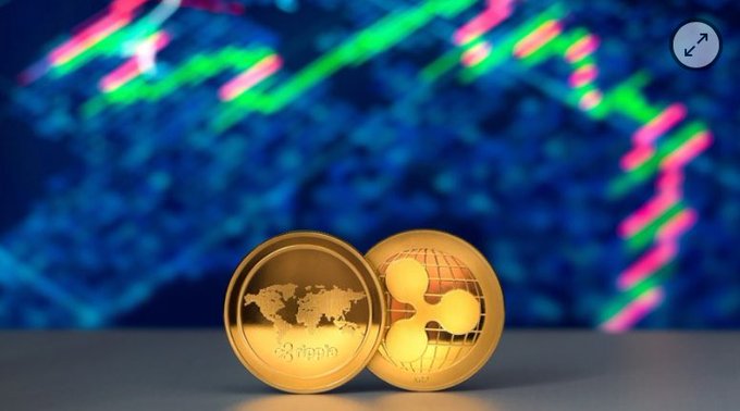 Two gold Ripple (XRP) coins, one displaying a world map and the other the XRP logo, placed in front of a blue background with blurred colorful stock market charts.