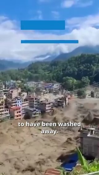 An aerial video screenshot shows a severe flood in a town near mountains, with muddy water sweeping through buildings and the caption 'to have been washed away.'