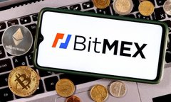 A blurry image of a tablet or framed display showing the BitMEX logo with its distinctive red and blue vertical bars next to the black text 'BITMEX', surrounded by wooden spoon utensils in the background.