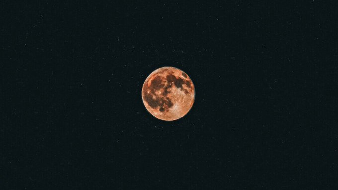 A photograph of a reddish-orange full moon centered against a dark, starry night sky.