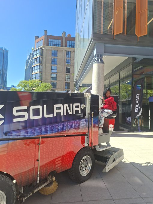 An orange street sweeper truck branded with the 'SOLANA' logo is parked outside a modern building, with a person in a red shirt sitting in the driver's seat.