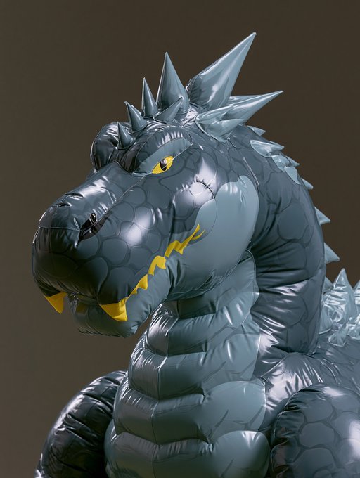 A close-up of an inflatable dark grey dragon or dinosaur toy with spikes, yellow eyes, and yellow flame accents on its neck.