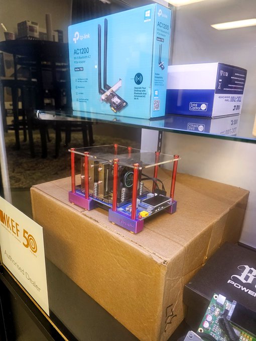 A TP-Link AC1200 Wi-Fi Bluetooth PCIe adapter box on a glass shelf above a cardboard box, with a purple 3D printer visible below.